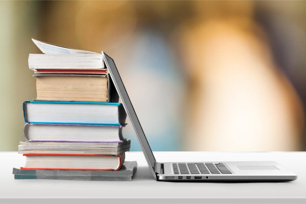 En trave böcker och en bärbar dator på ett bord